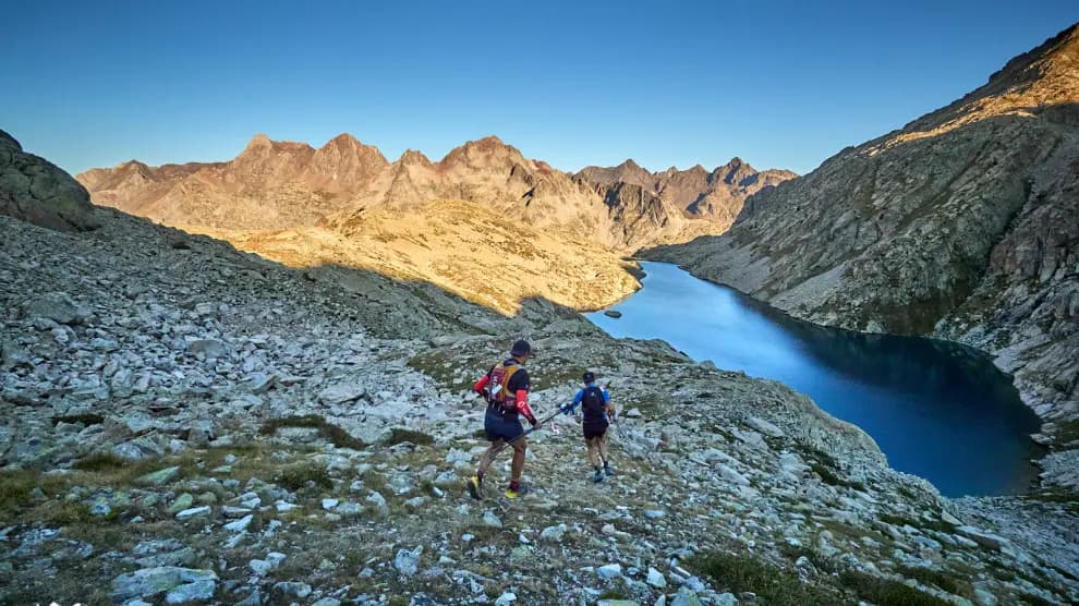 Corredores corriendo por un paisaje de alta montaña con un lago en los Pirineos